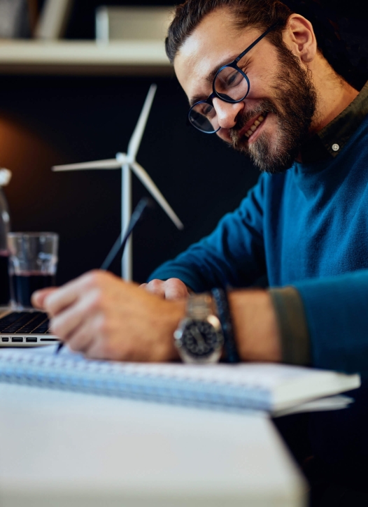 Young smiling dedicated engineer sitting in his office and drawing new prototype of windmill. Sustainable development concept.